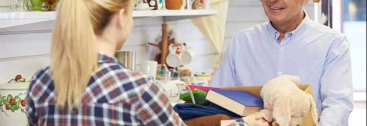 Zwei Personen in einem Laden, eine Person reicht der anderen eine Kiste.